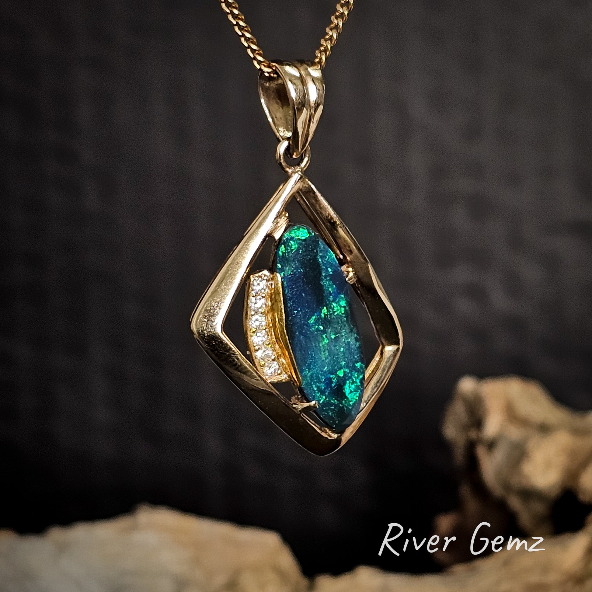 Gold pendant with diamonds and an oval shaped green and blue black opal on a dark background, featuring 'River Gemz' branding.
