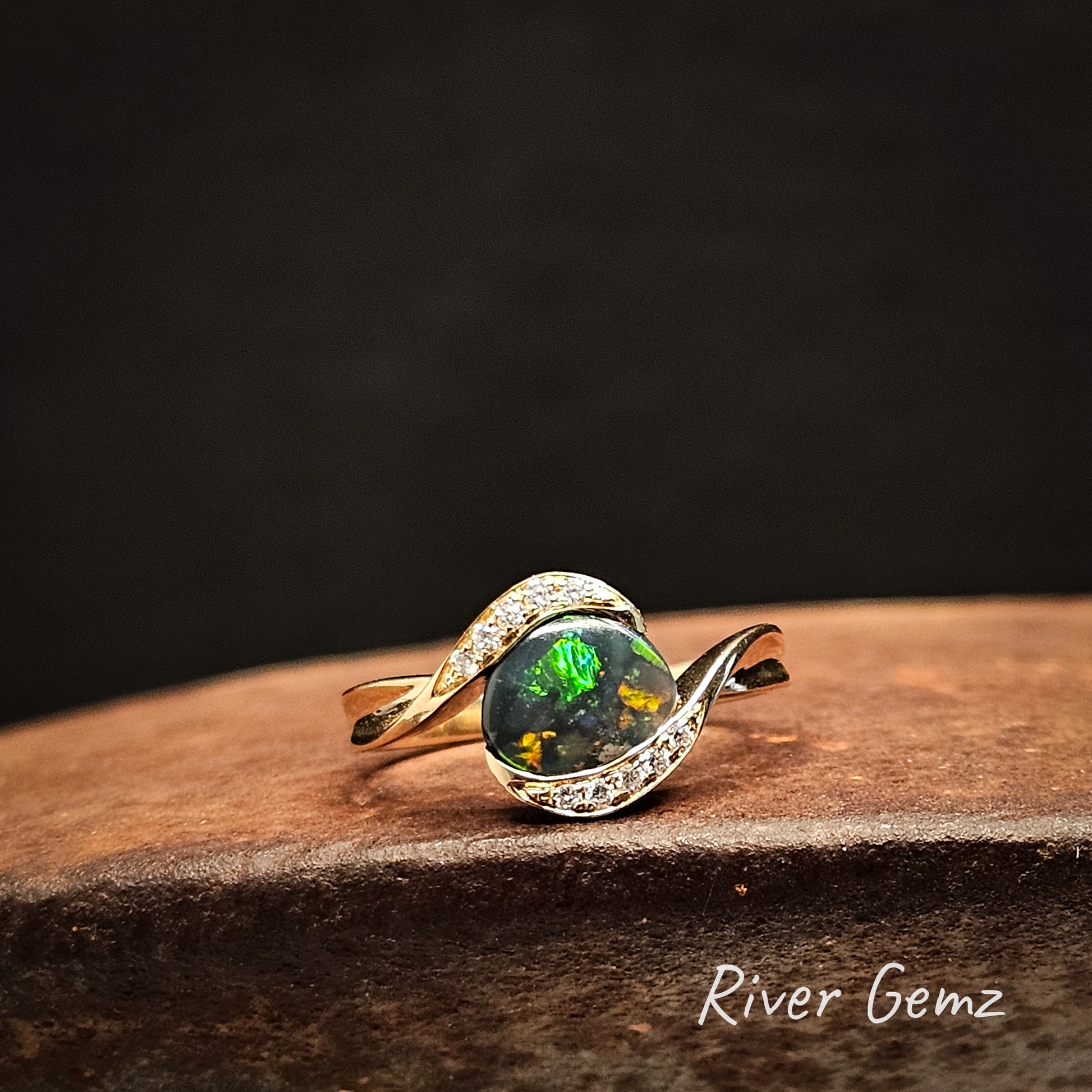 Gold ring with a green gemstone on a dark background, featuring the brand 'River Gemz'.