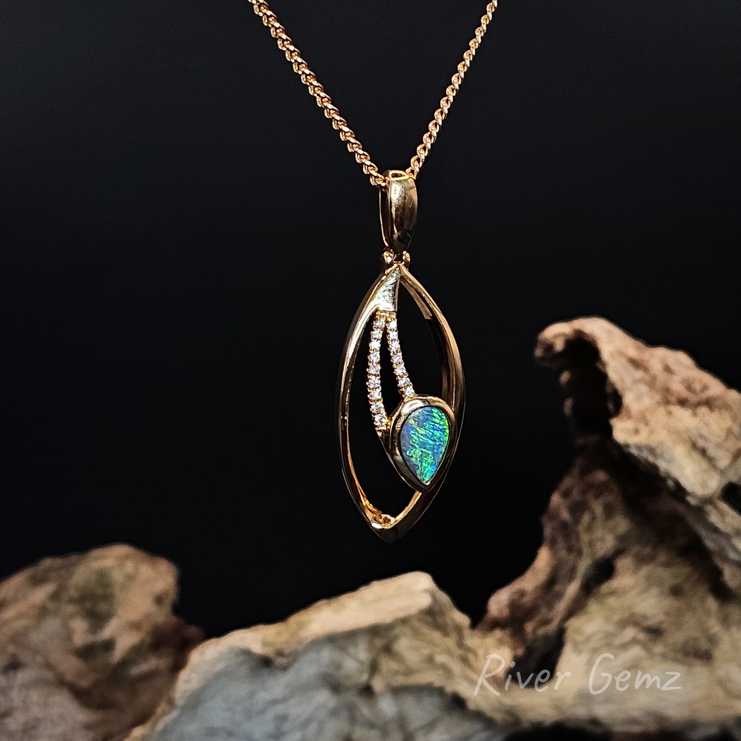 Gold pendant with an inverted tear drop shaped dark opal and diamonds on a dark background