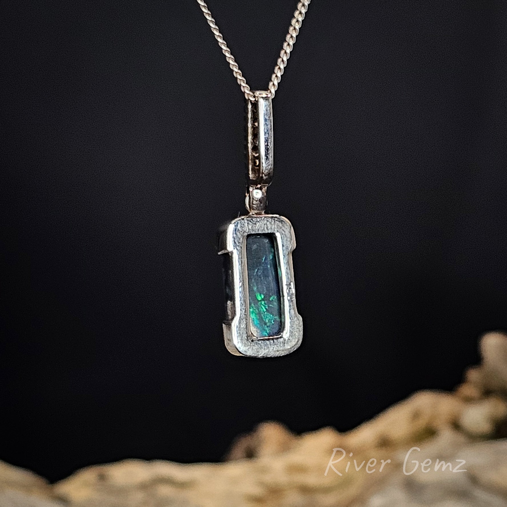Rear view of the necklace shows the dark base tone of the included black opal on a dark background, featuring 'River Gemz' branding.