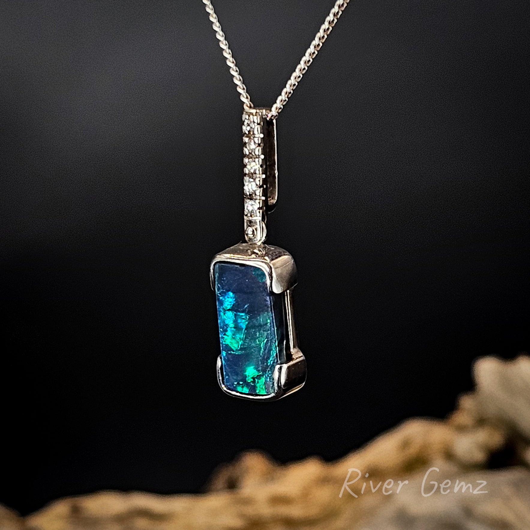 Black opal partial besel set in white gold pendant with diamonds in the bail and silver chain on a dark background