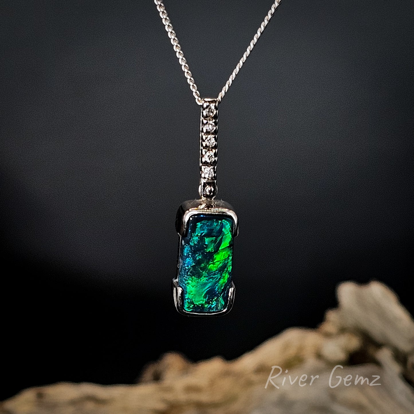 Necklace with a green and blue black opal and 5 channel set diamonds on a dark background with 'River Gemz' branding.