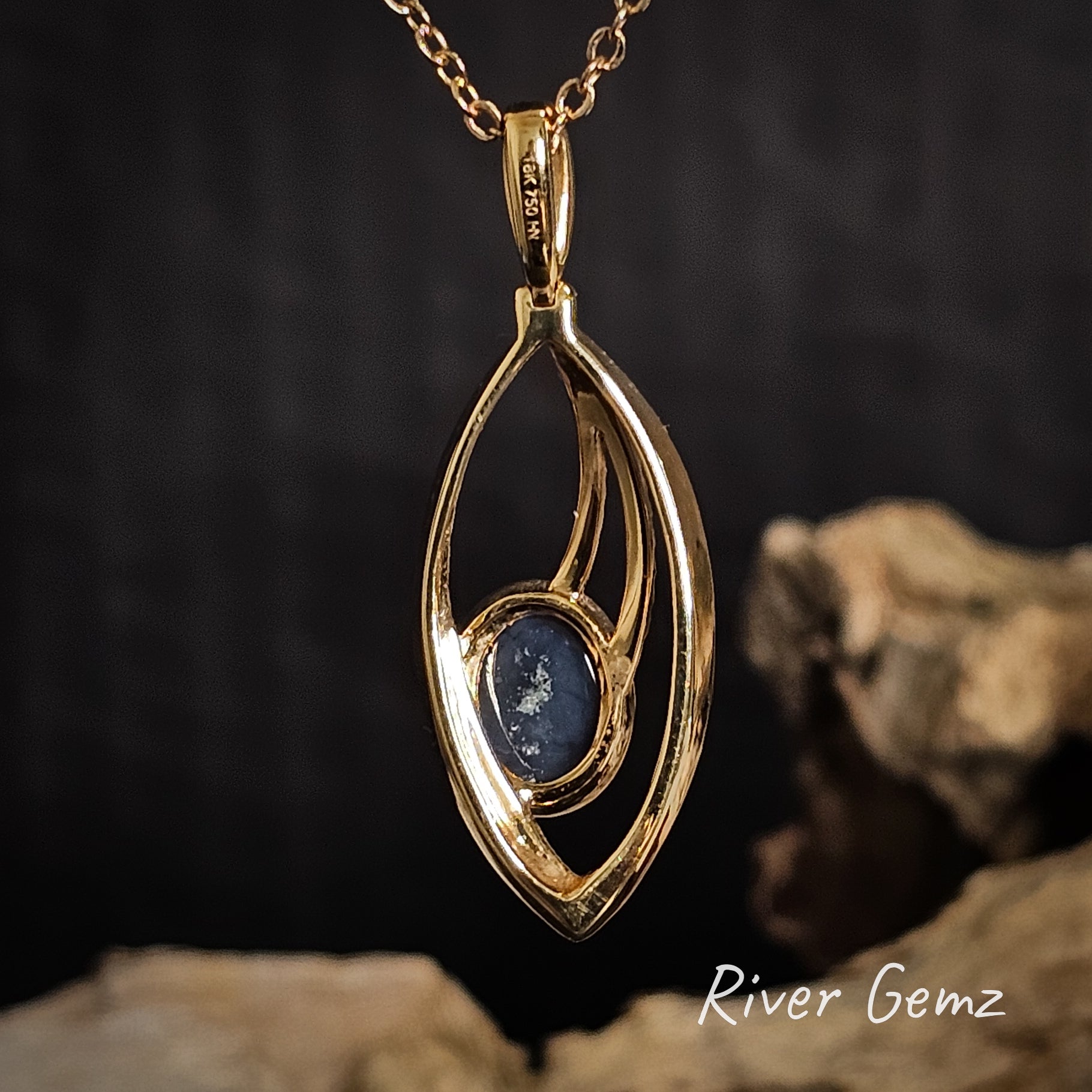 Back of gold pendant showing the dark base tone of the black opal set in it on a dark background with 'River Gemz' branding.