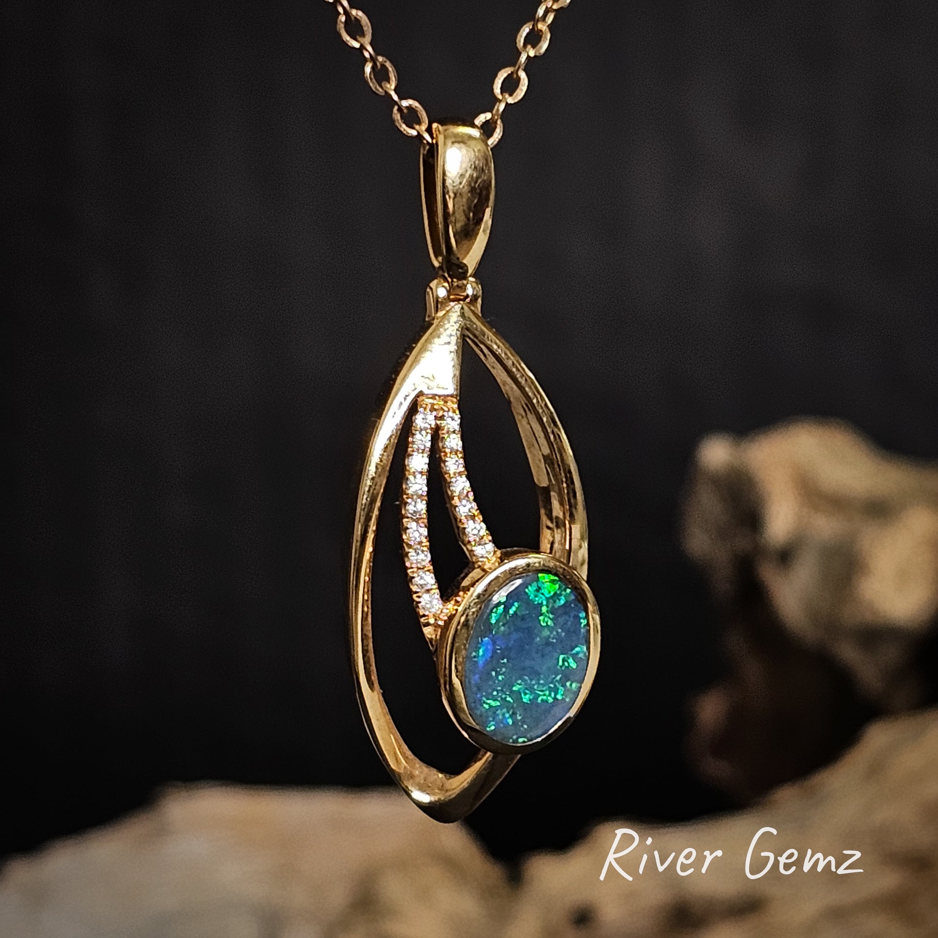 Gold pendant with two strands of diamonds and a black opal on a dark background, featuring 'River Gemz' branding.