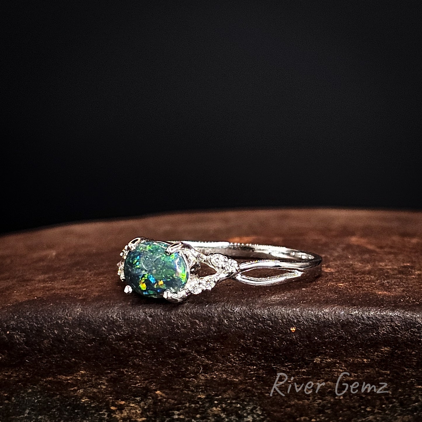 White gold ring with a green black opal and diamonds on a dark surface, featuring 'River Gemz' branding.