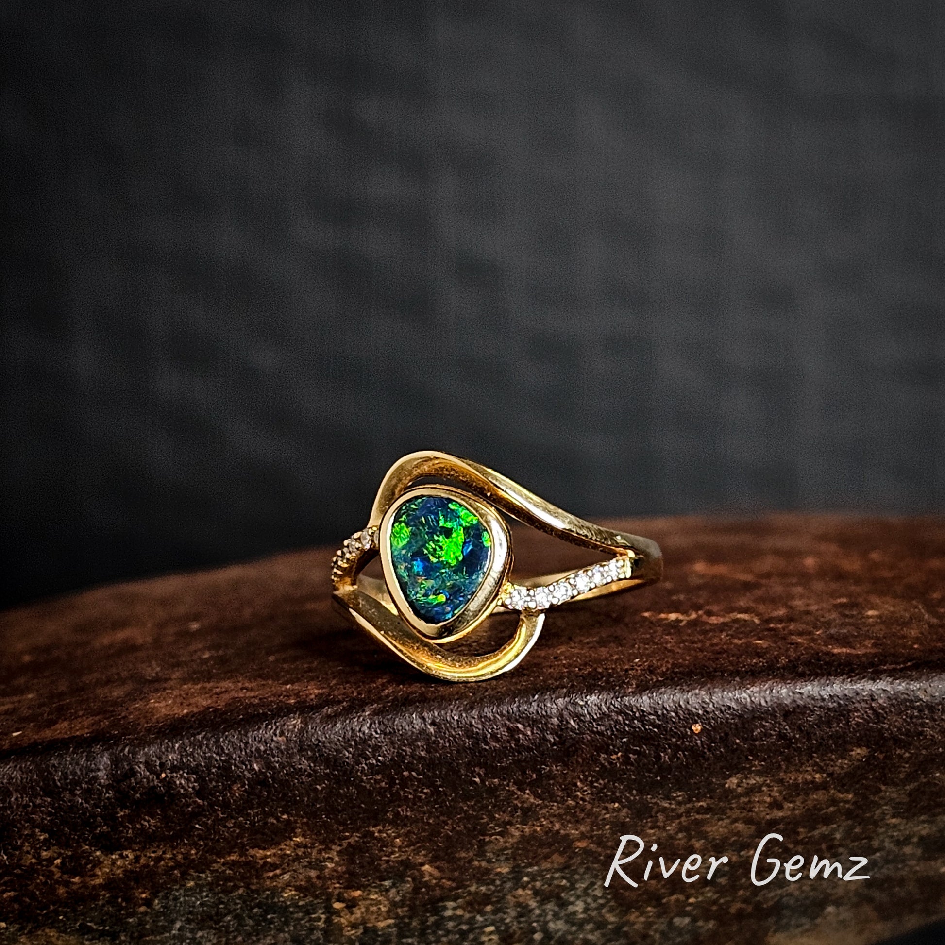 Green and blue black opal besel set in yellow gold ring with white diamonds on the shoulders.