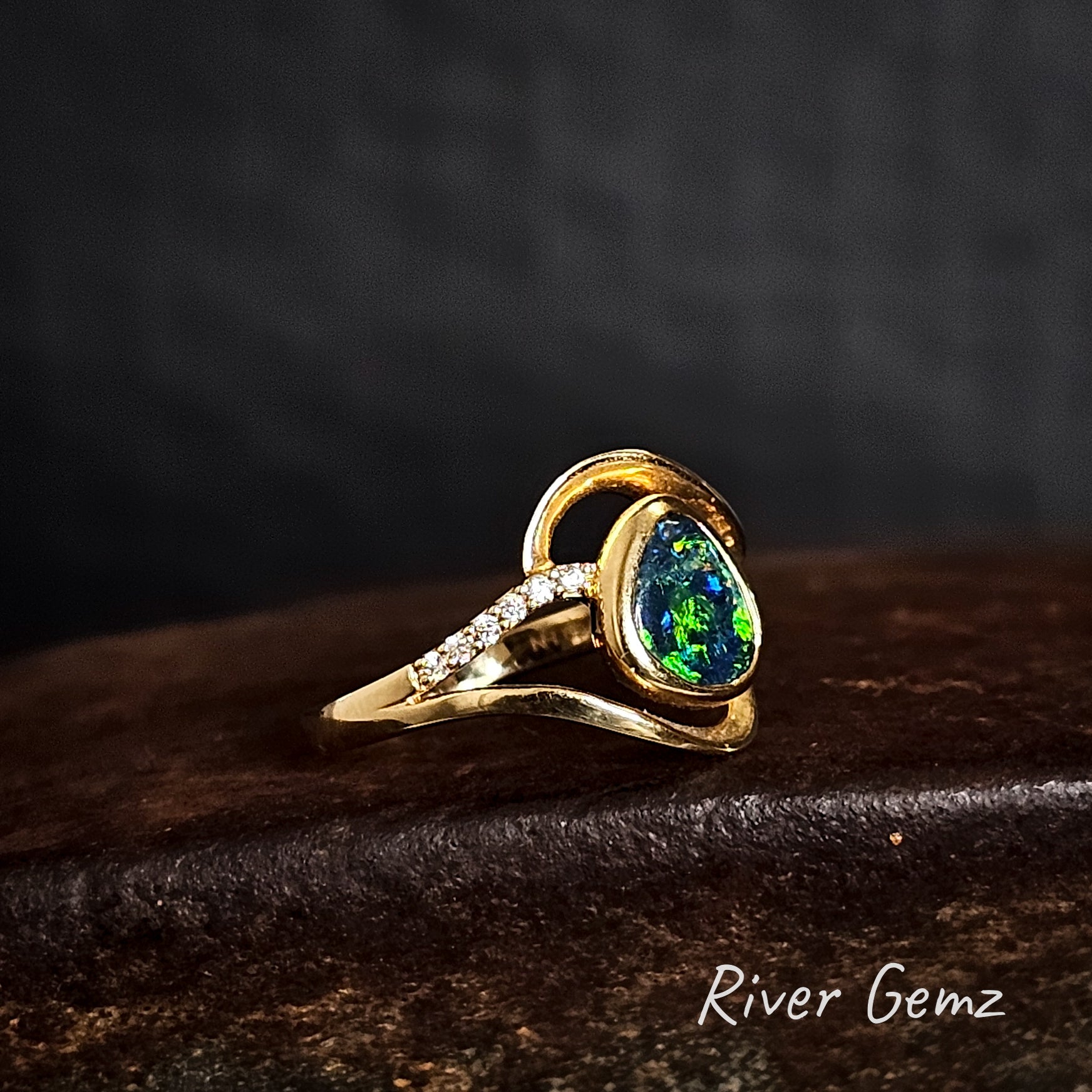 Green dark opal besel set in yellow gold ring which has a row of 6 small white diamonds on both shoulders of the ring.