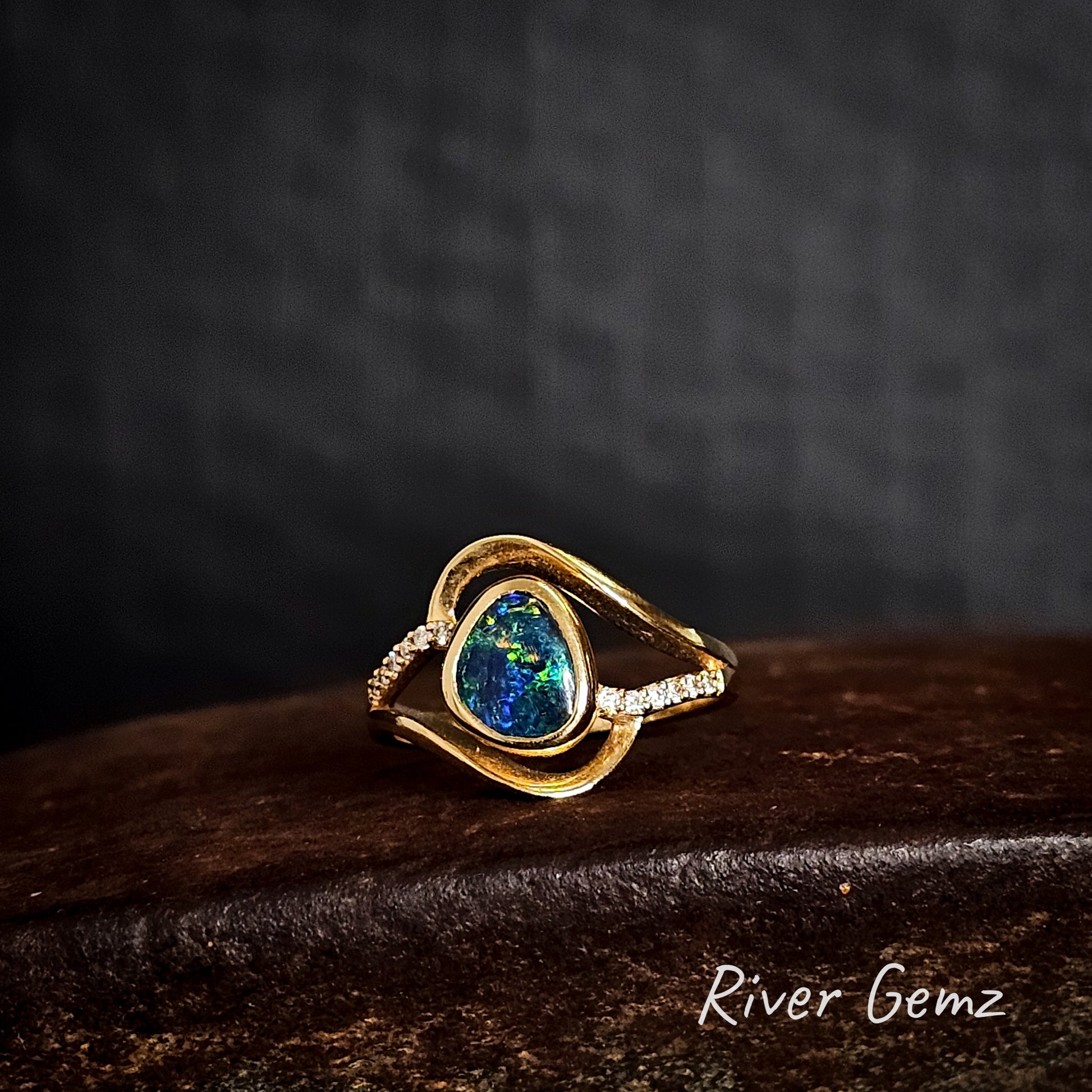 Blue and green black opal set in a yellow gold ring with numerous white diamonds.