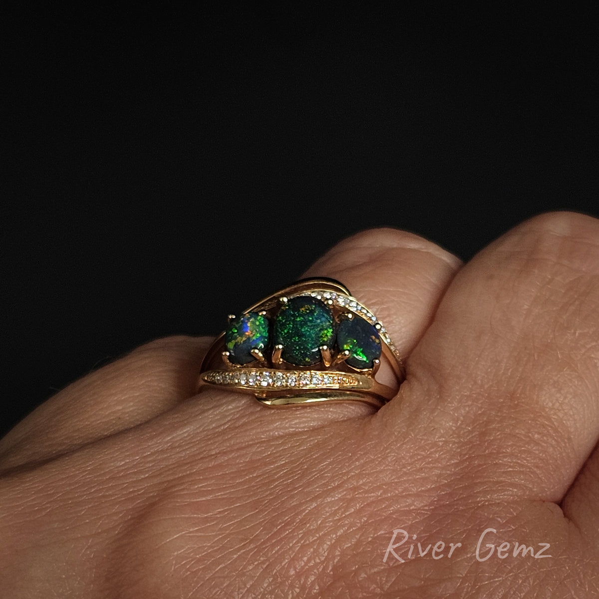 Trilogy opal and diamond ring worn on left hand ring finger against a black background with 'River Gemz' watermark in the bottom right hand corner.