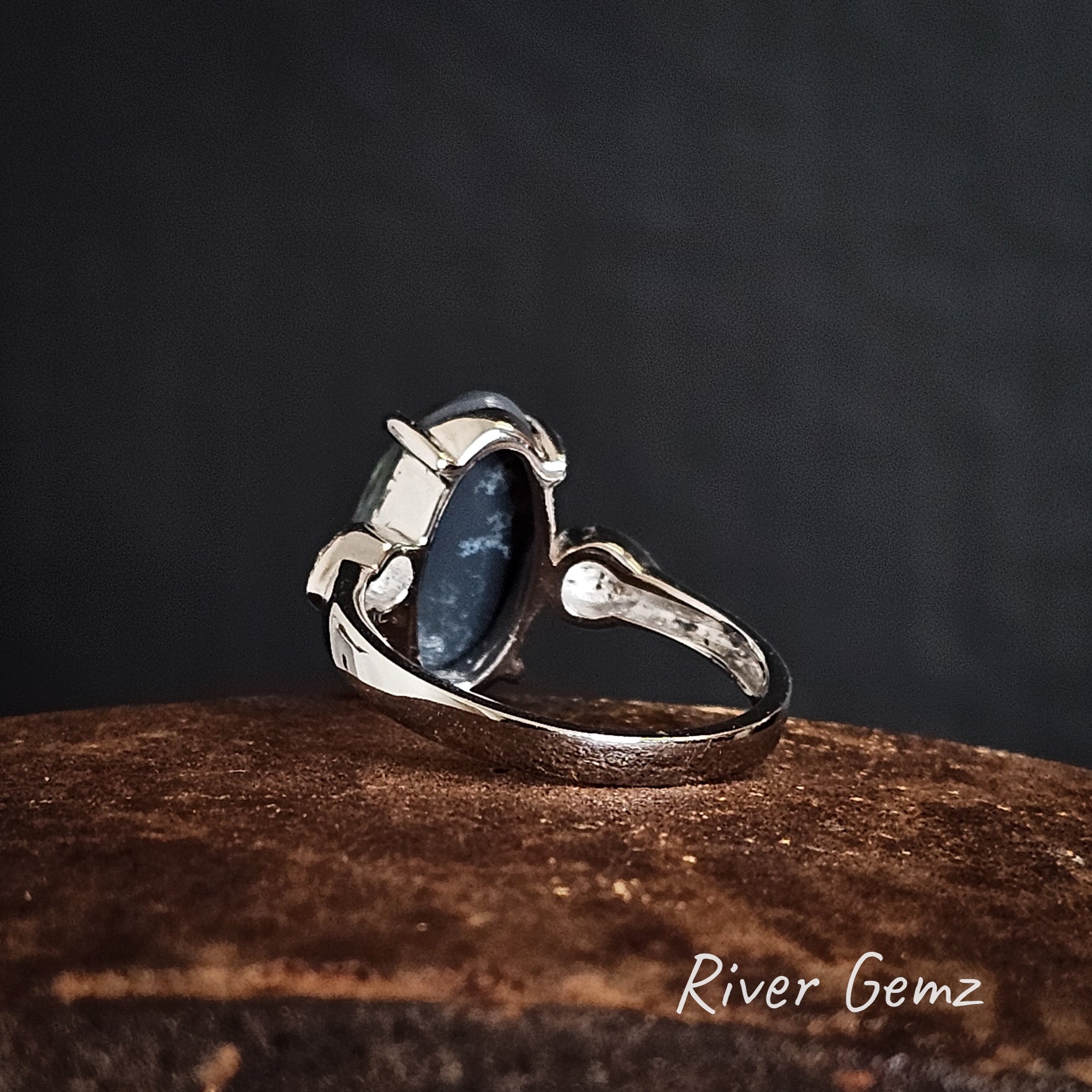 Back of white gold ring showing the dark base of the black opal on a rusty coloured surface, branded 'River Gemz'.