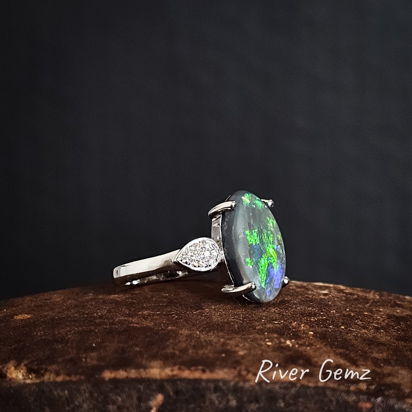 Side view of white gold ring with an opal stone on a dark background, branded 'River Gemz'.