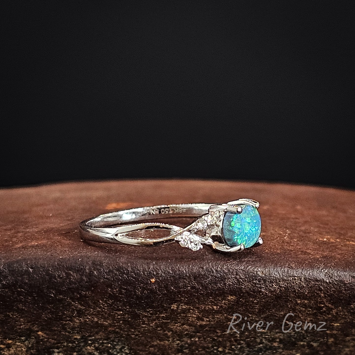 Side view of white gold ring showing the 18K stamp, the uniform thickness of the black opal and the twist design on the ring's shoulders.