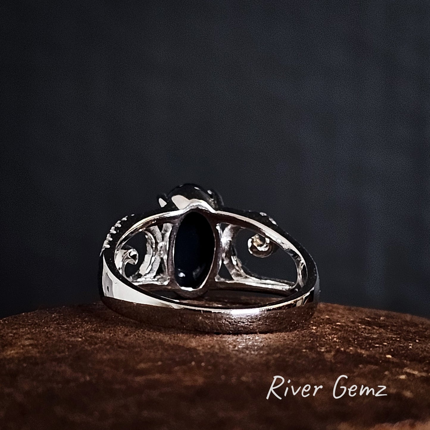 Back view of the white gold ring showing the dark base of the black opal on a dark background, branded 'River Gemz'.