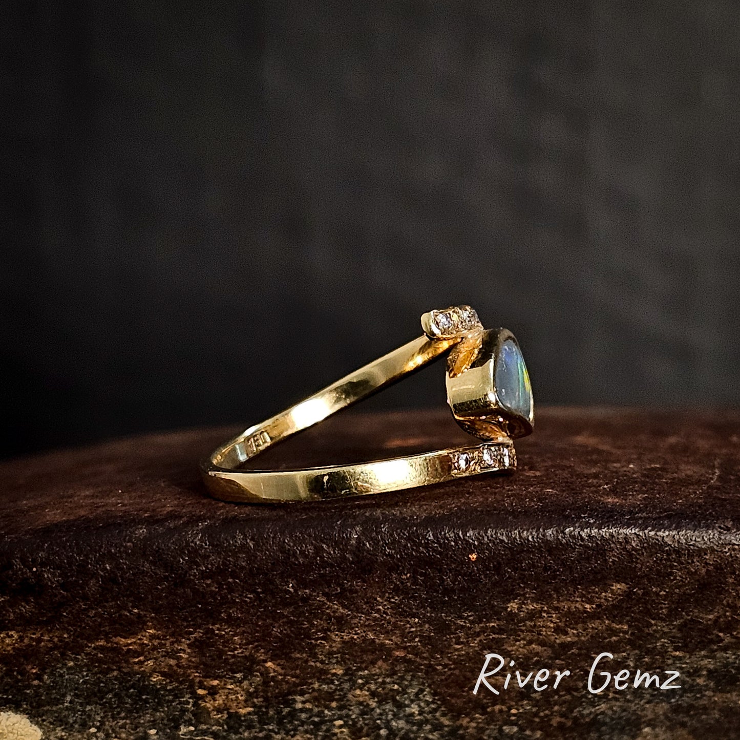 Side view of gold ring with an opal stone and some diamonds on a dark background, branded 'River Gemz'.
