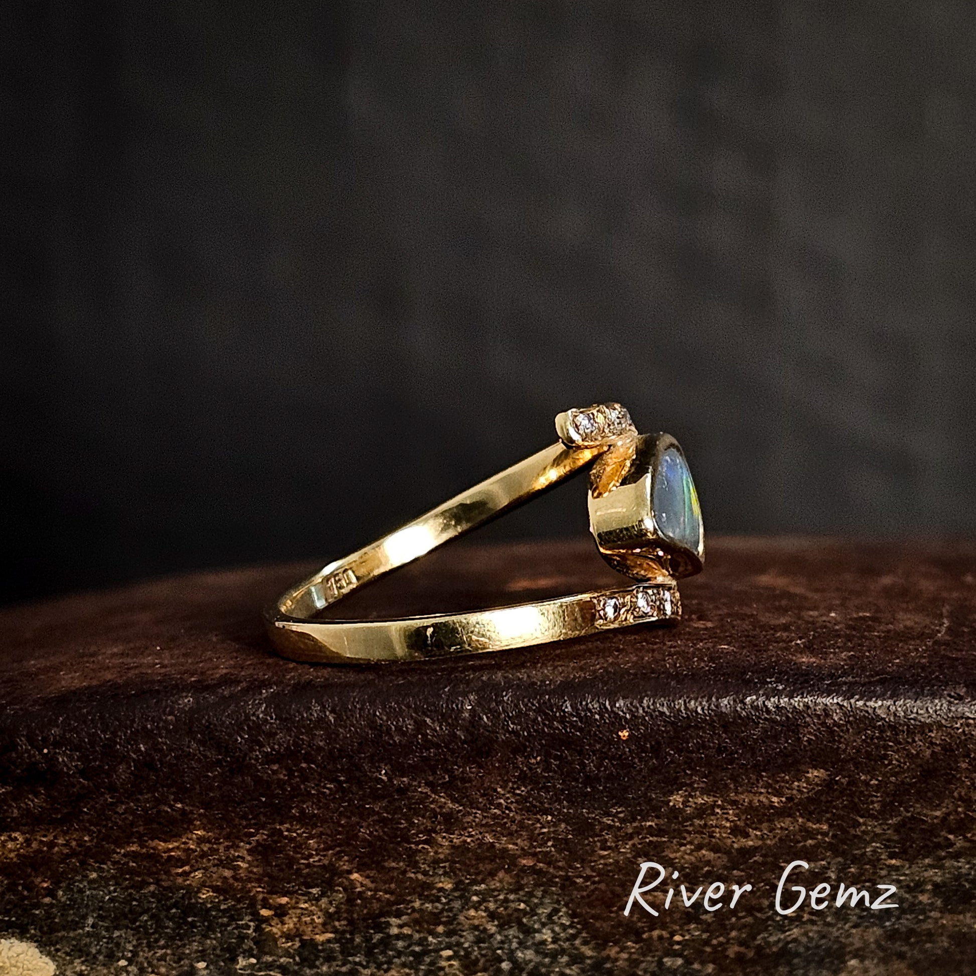 Side view of gold ring with an opal stone and some diamonds on a dark background, branded 'River Gemz'.