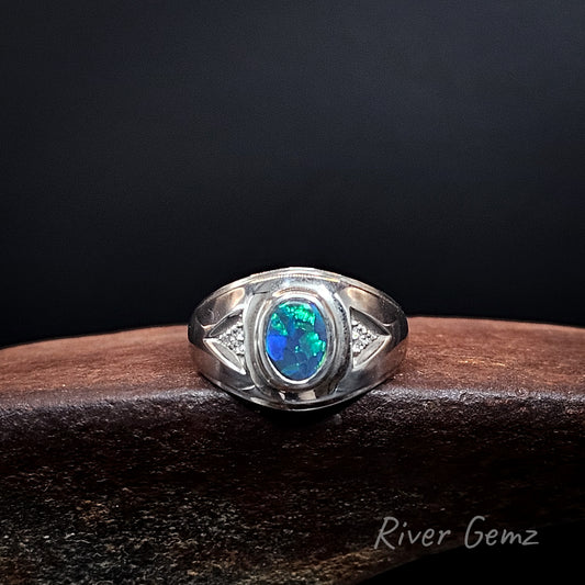 A sterling silver ring featuring an oval-cut blue opal gemstone, displayed on a dark wooden block against a black background. The brand name 'River Gemz' is visible as a watermark in the bottom right corner.