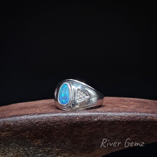 A sterling silver signet ring featuring a vibrant blue teardrop-shaped opal and a small triangle of 3 diamonds on the band, displayed on a dark brown wooden block against a black background.
