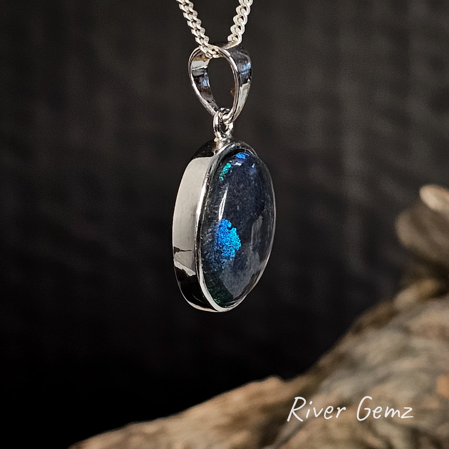 Black opal besel set in silver necklace with a large bail on a dark background, featuring 'River Gemz' branding.