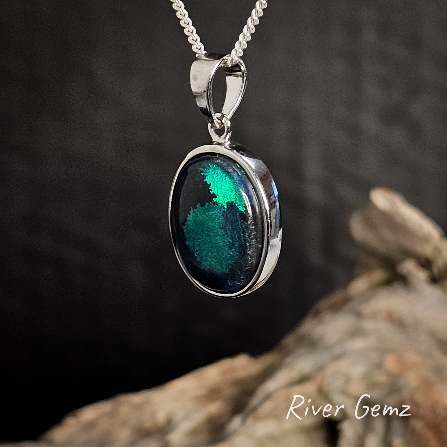 Silver pendant with a green and black stone on a dark background, featuring 'River Gemz' branding.