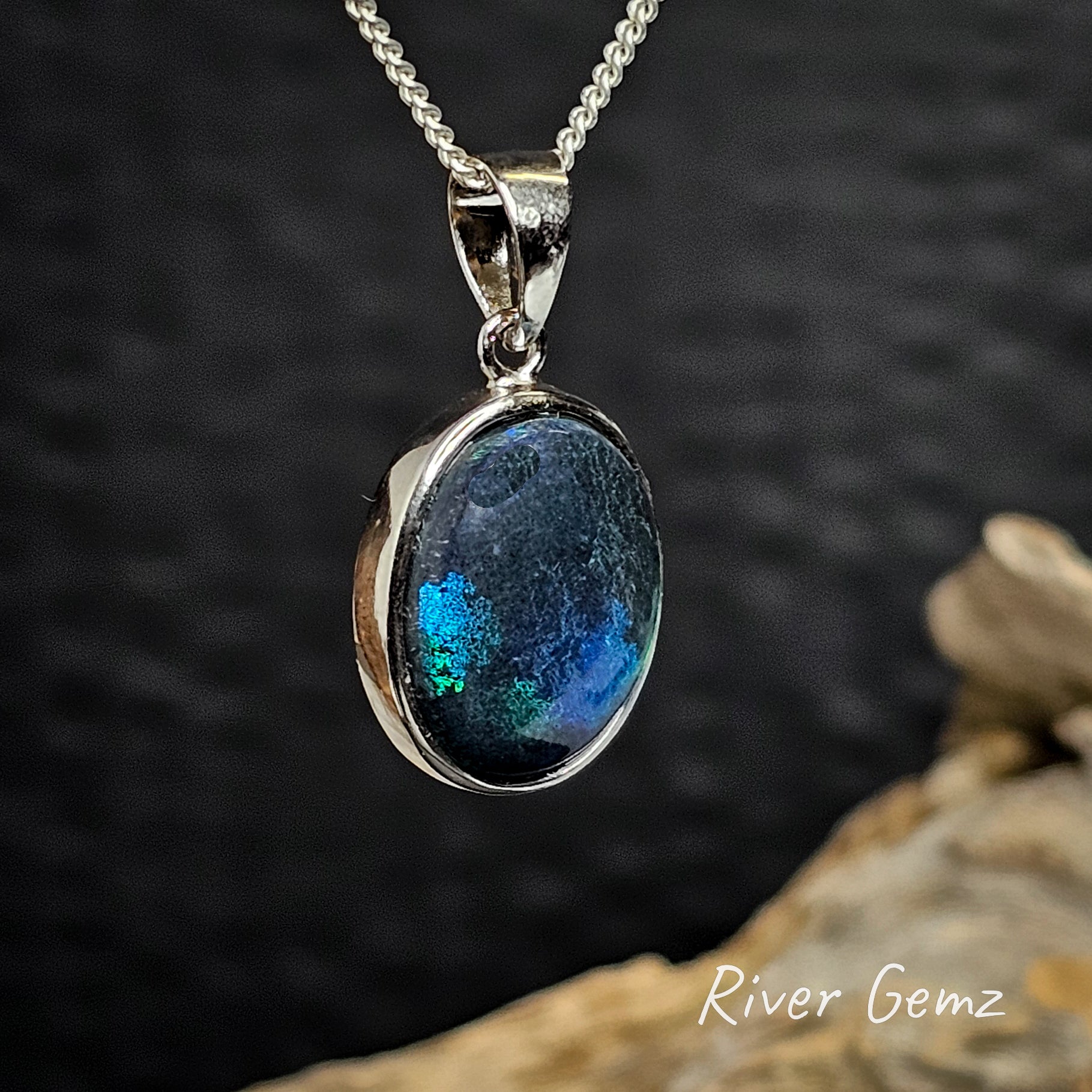 Silver pendant with a blue black opal a dark background.
