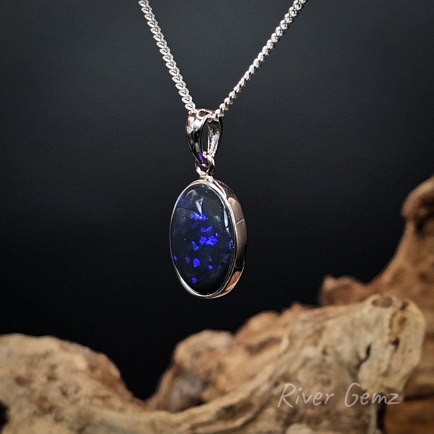 Silver pendant with an oval shaped dark blue opal on a dark background
