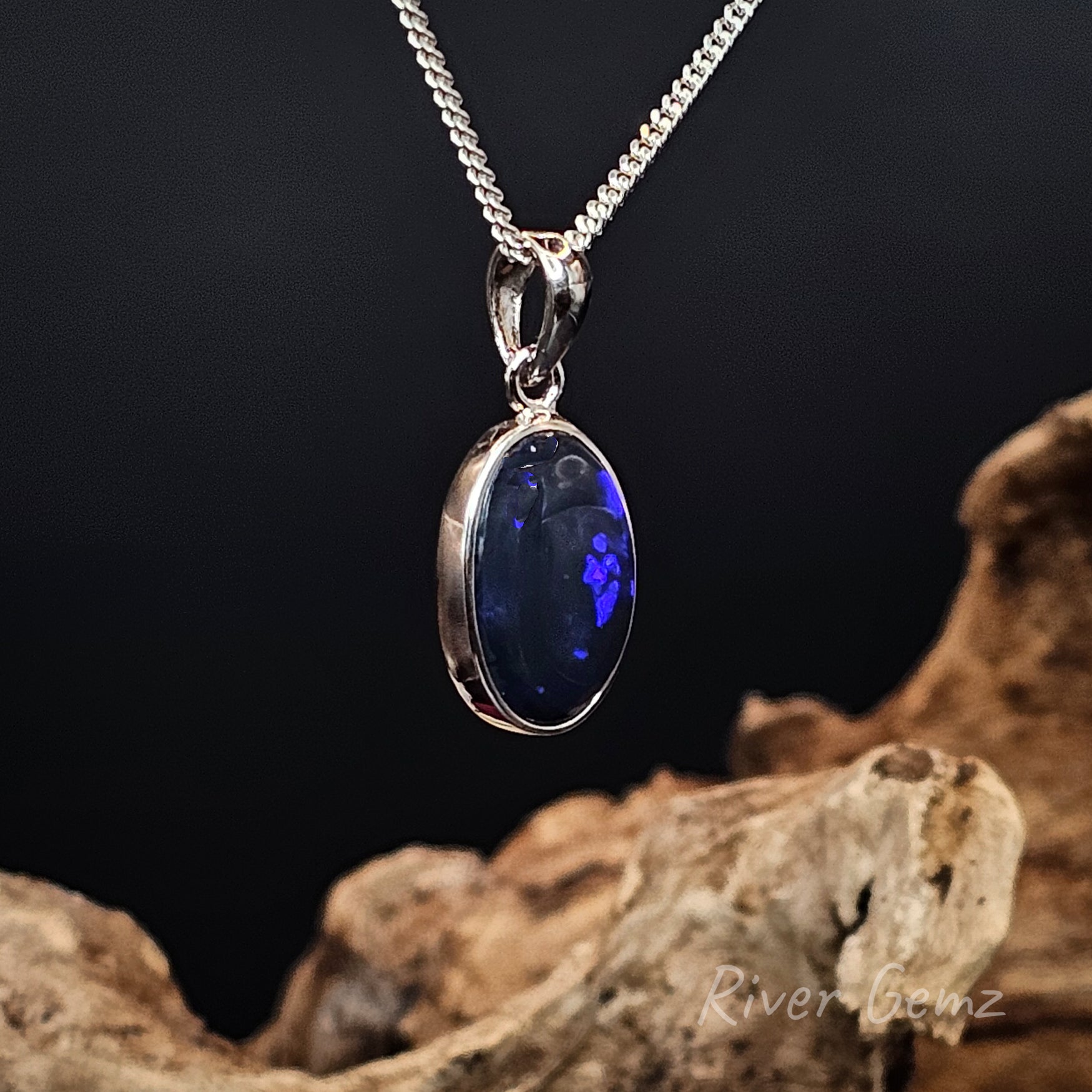 Silver pendant with a besel set black opal with blue splashes of colour on a dark background