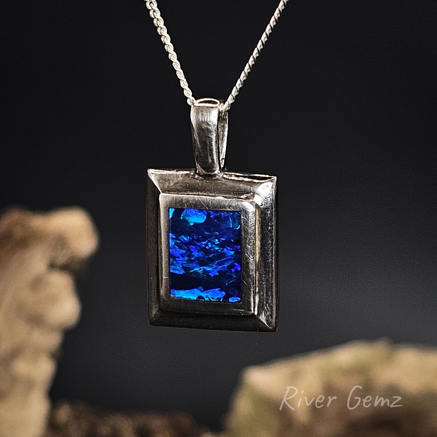 Silver pendant with blue black opal on a dark background, featuring 'River Gemz' branding.
