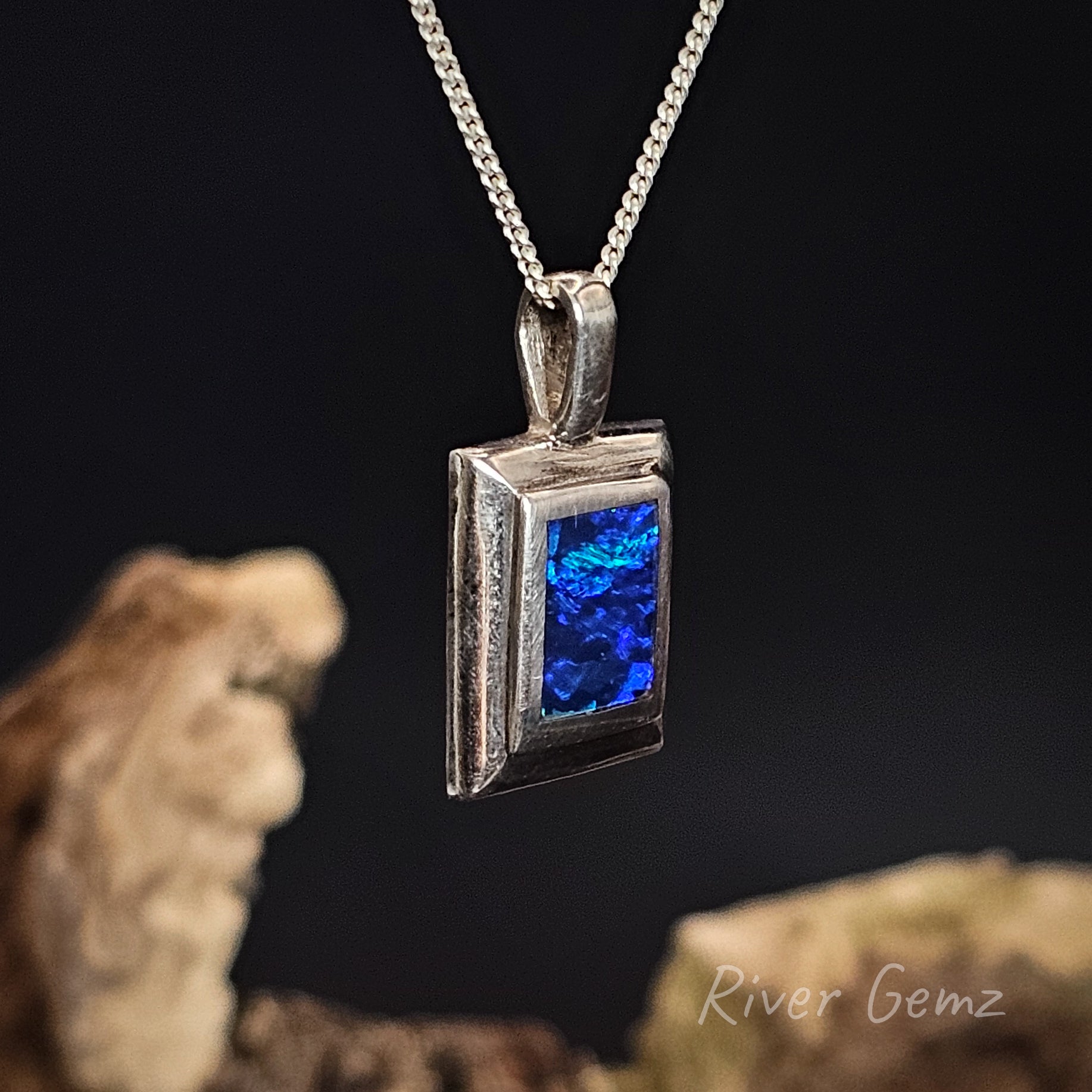 Silver necklace with a rectangular blue dark opal on a chain against a dark background
