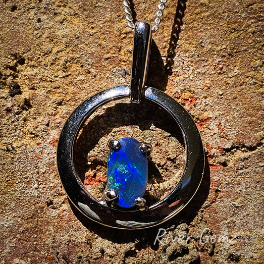 Round silver necklace with dark blue and green oval shaped opal.