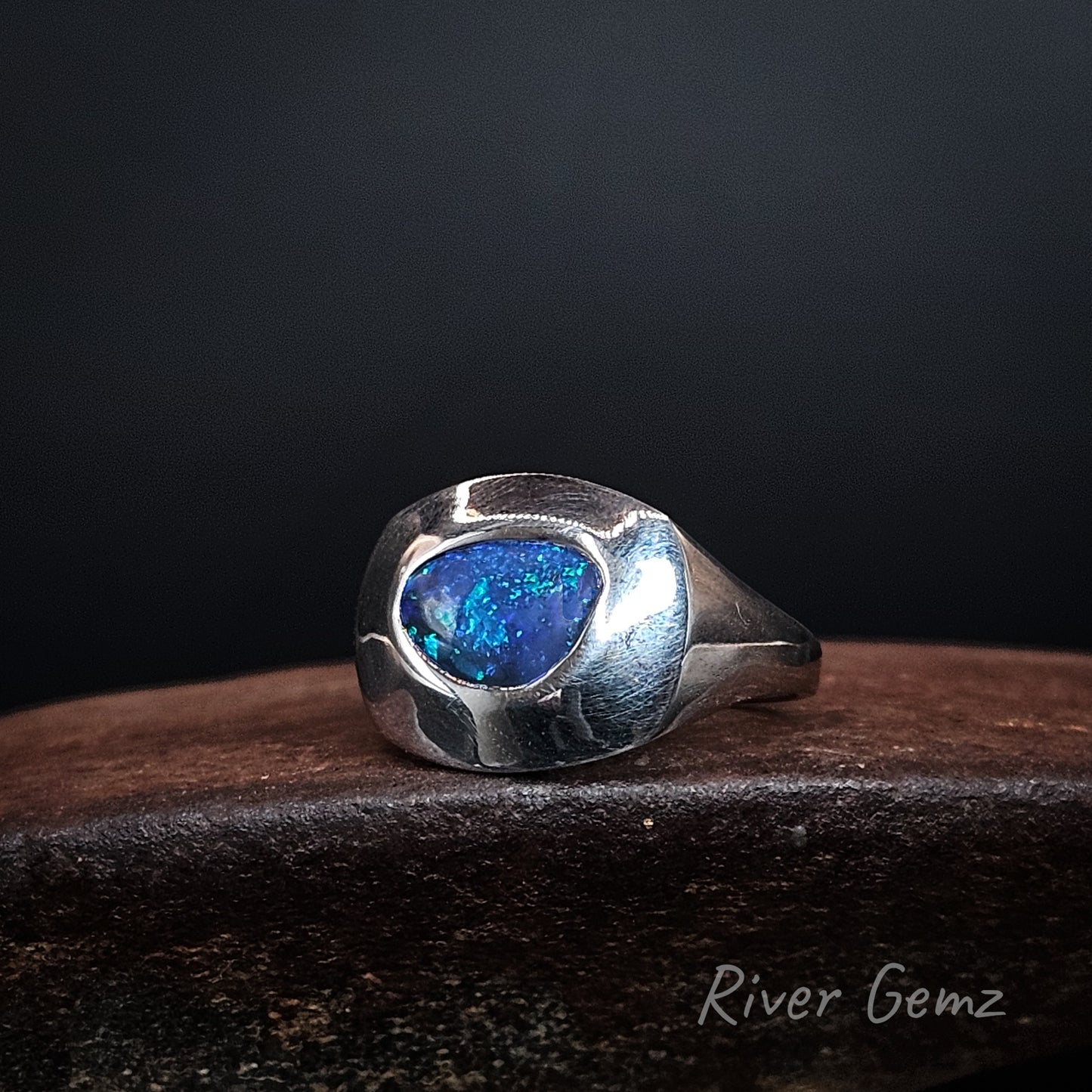 Round cornered blue coloured black opal fully besel set in sterling silver ring with tapered shoulders.