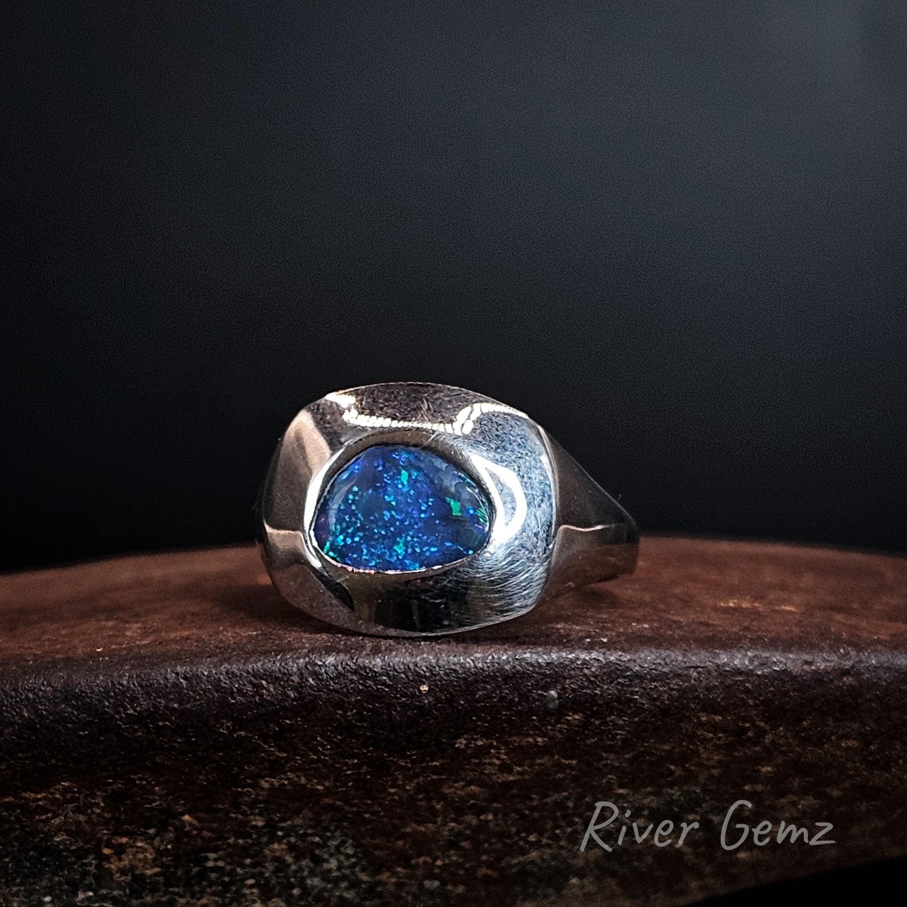 Blue coloured black opal set in wide beselled sterling silver ring.