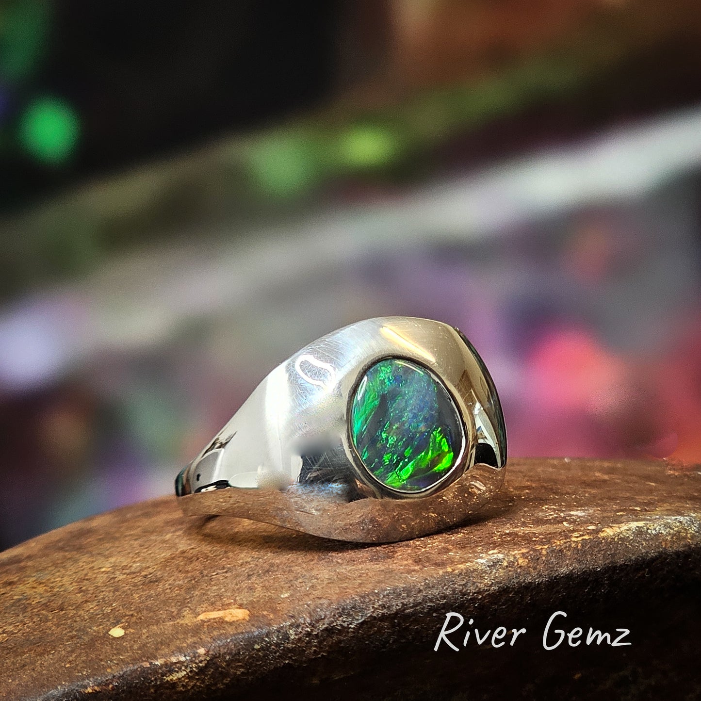 The design is reminiscent of an old anode TV with the opal as the TV screen. Black opal cut as an imperfect circle with vivid greens in silver ring.