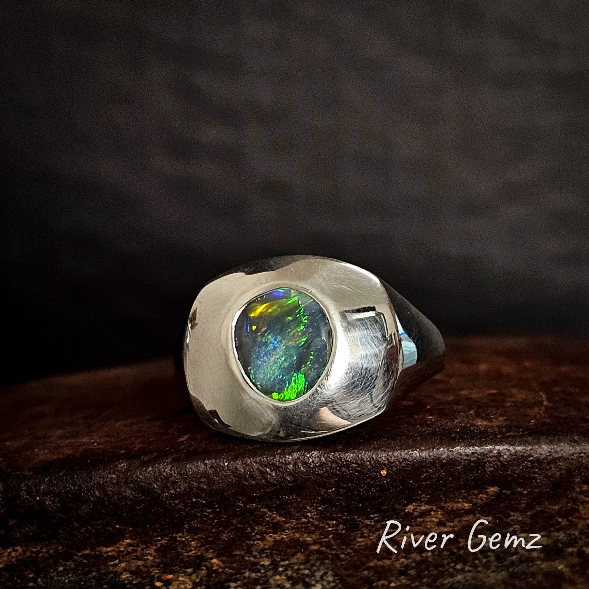 Silver ring with a colorful black opal on a dark background, featuring the brand 'River Gemz'.