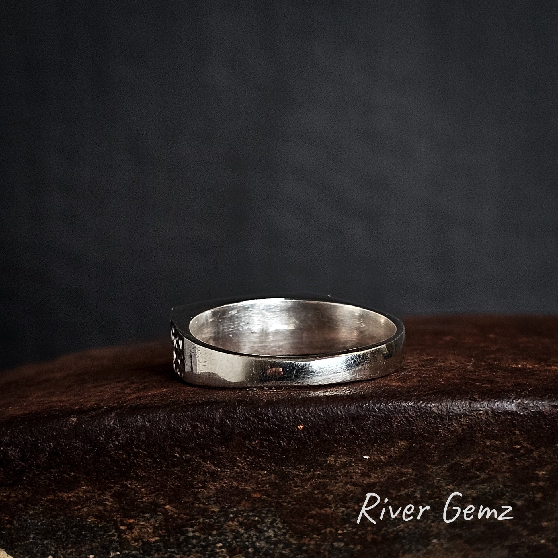 Rear view of silver ring on a cast iron surface with 'River Gemz' branding.