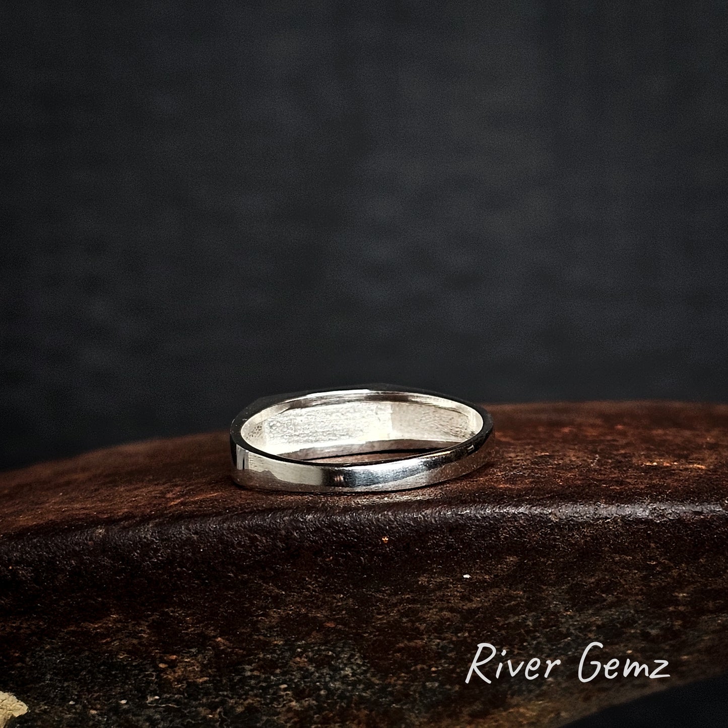 Rear view of silver ring on a rusty brown surface with 'River Gemz' branding.