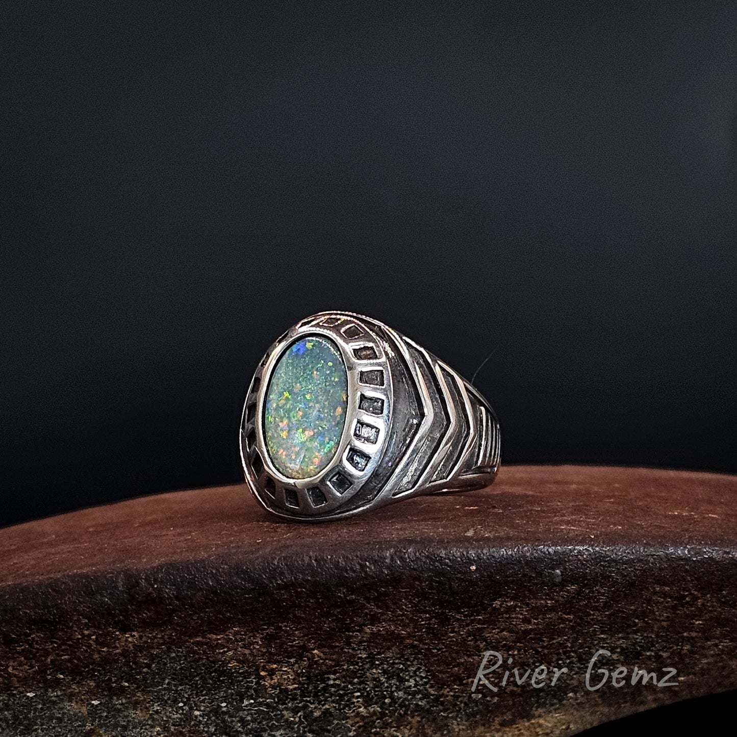 Silver ring with numerous ridges, tapered shoulders and besel set colourful dark opal.