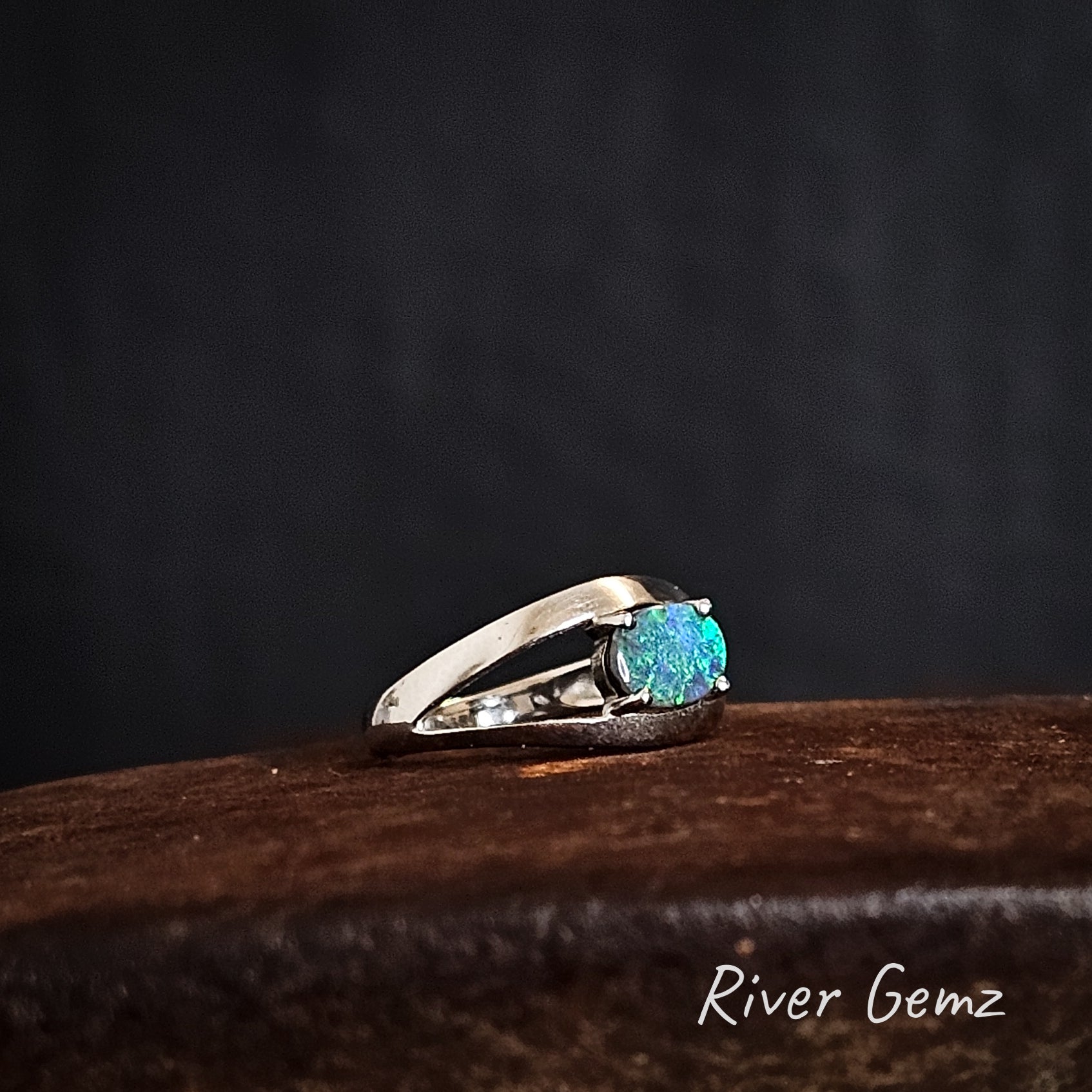 Silver ring with a blue and green black opal on a dark background, featuring 'River Gemz' branding.