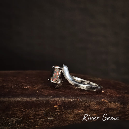 Side view of silver ring showing the thickness of the black opal on a dark cast iron surface, 'River Gemz' brand visible.