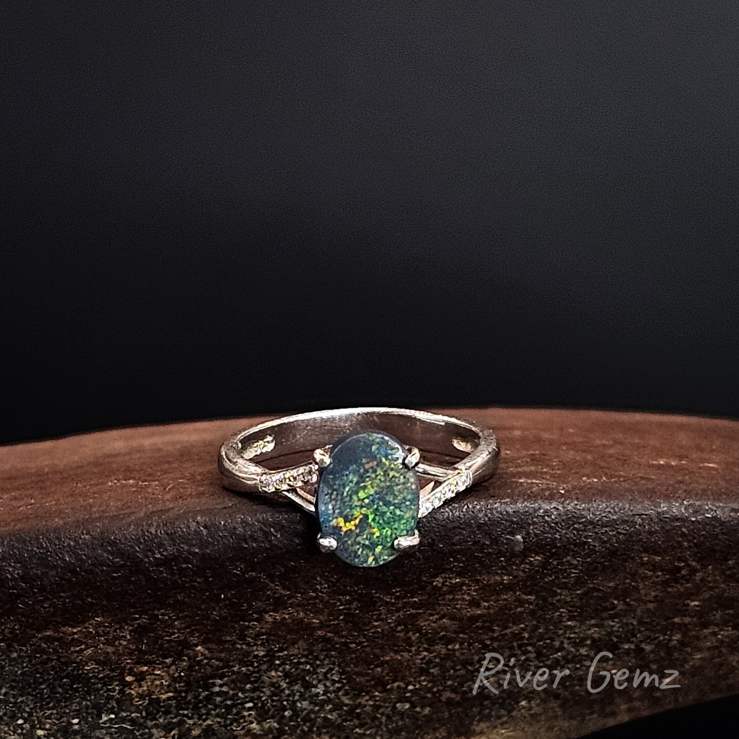 Oval shaped dark opal claw set in sterling silver ring with white topaz stones on each shoulder.