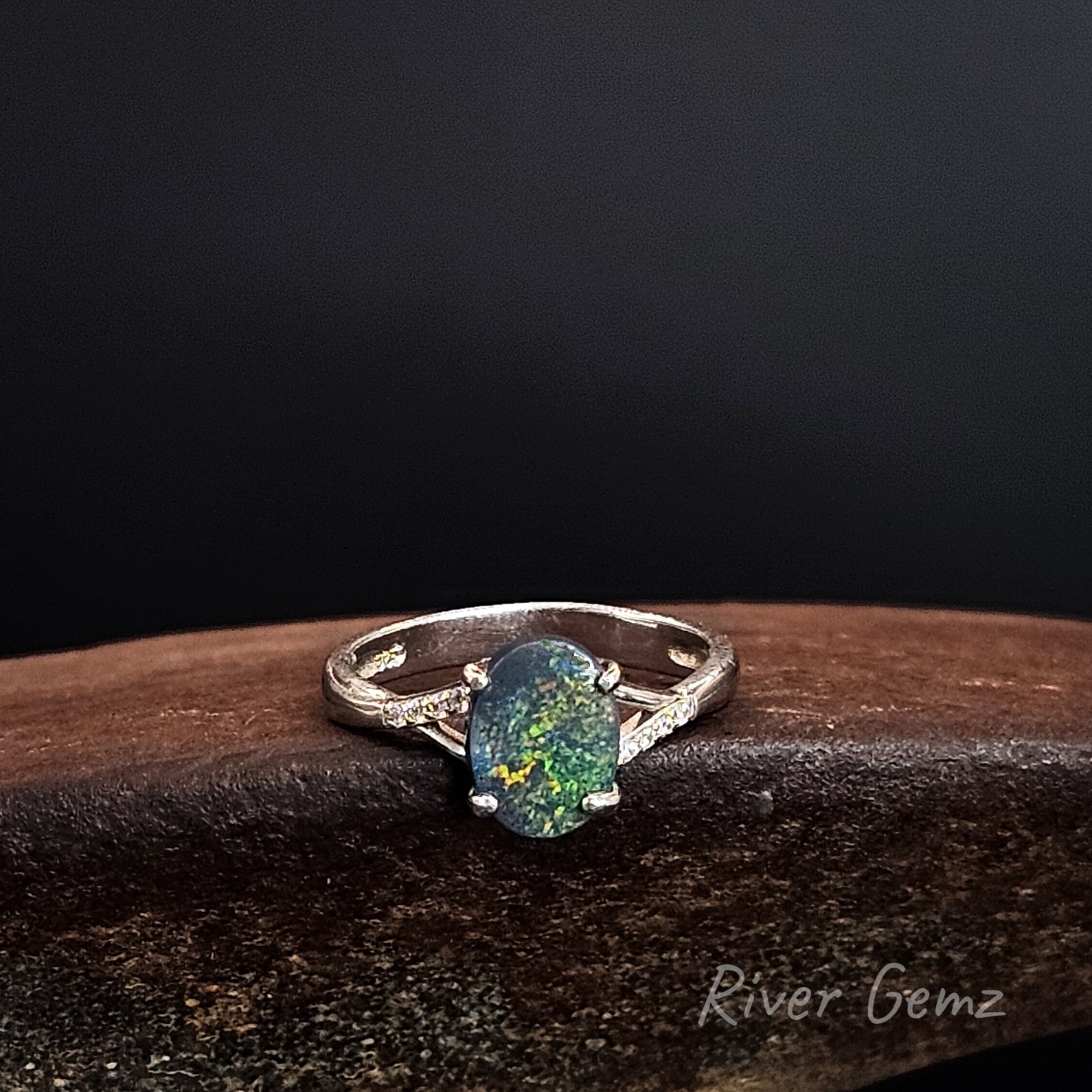 Oval shaped dark opal claw set in sterling silver ring with white topaz stones on each shoulder.