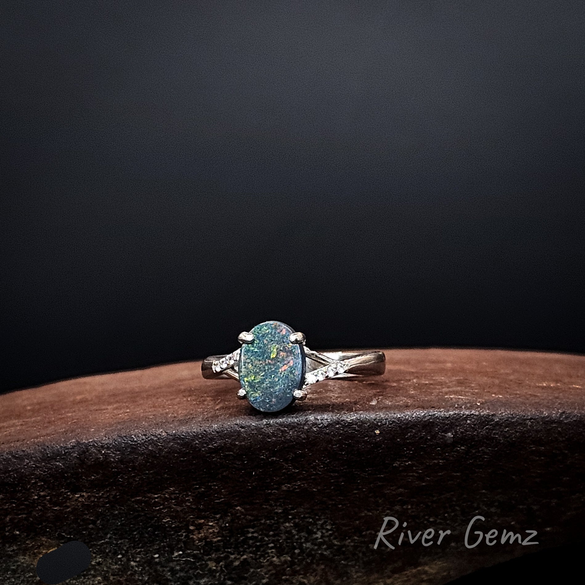 Oval shaped black opal with multi-colours claw set in silver ring.