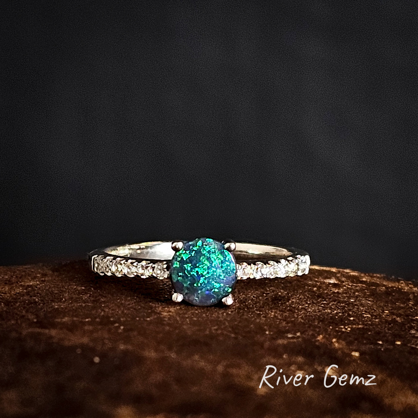 Ring with a blue and green black opal on a dark background, branded 'River Gemz'.