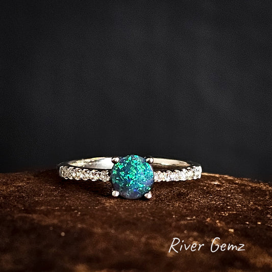 Ring with a blue and green black opal on a dark background, branded 'River Gemz'.