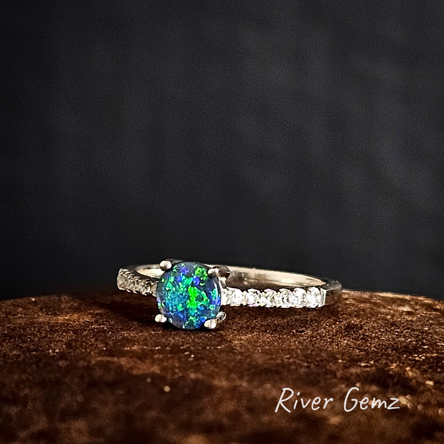 Ring with a blue and green round 5 mm gemstone on a dark background, branded 'River Gemz'.