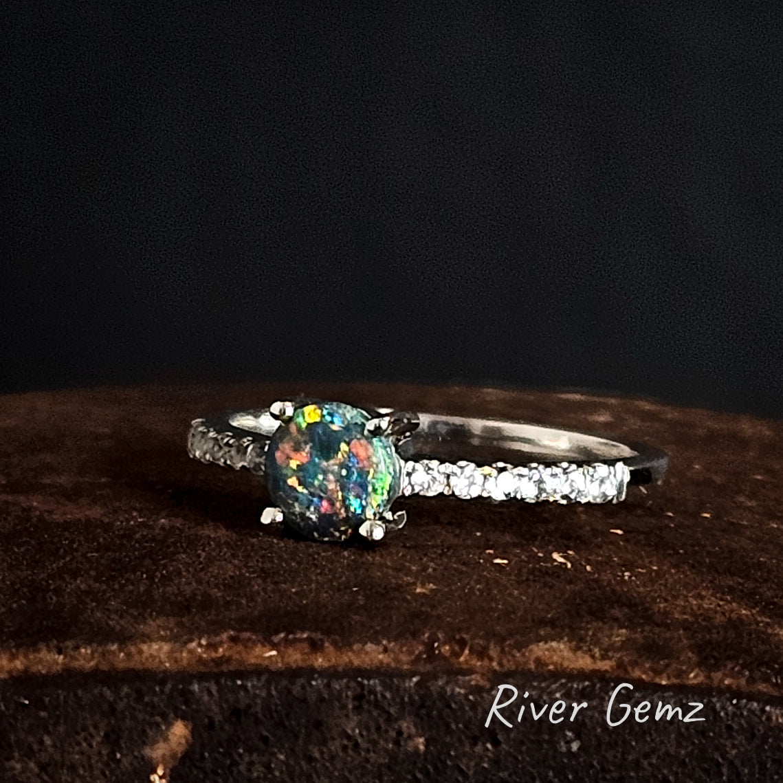 Sterling Silver ring with a colorful black opal and topaz shoulders on a dark background, branded 'River Gemz'.