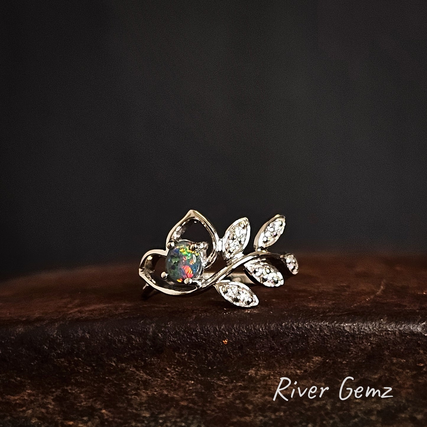 Silver ring with black opal and white topaz stones on a dark background, featuring 'River Gemz' branding.