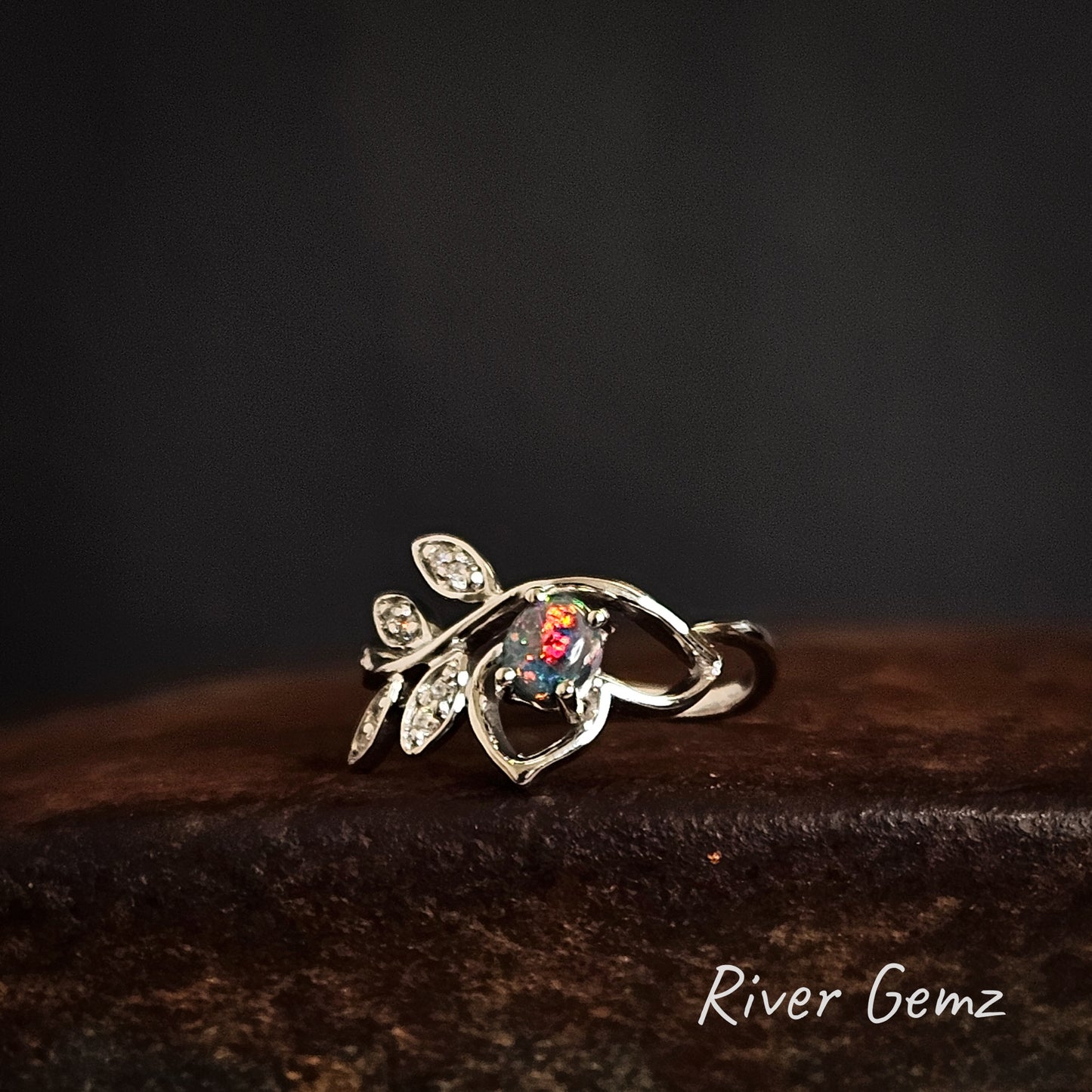 Silver ring with gemstone on a dark background, featuring 'River Gemz' branding.