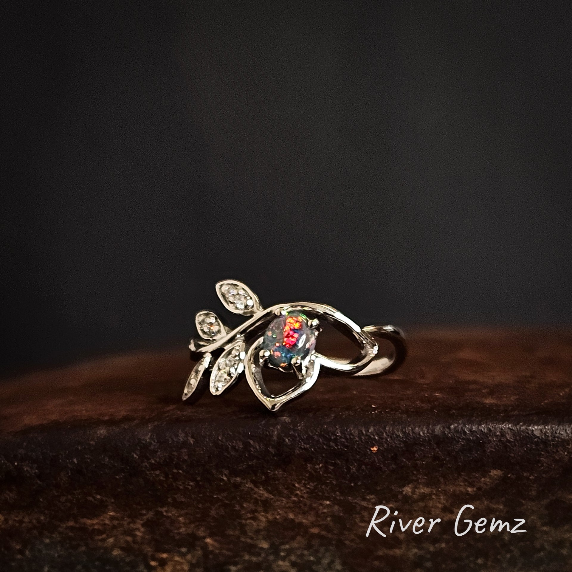 Silver ring with gemstone on a dark background, featuring 'River Gemz' branding.