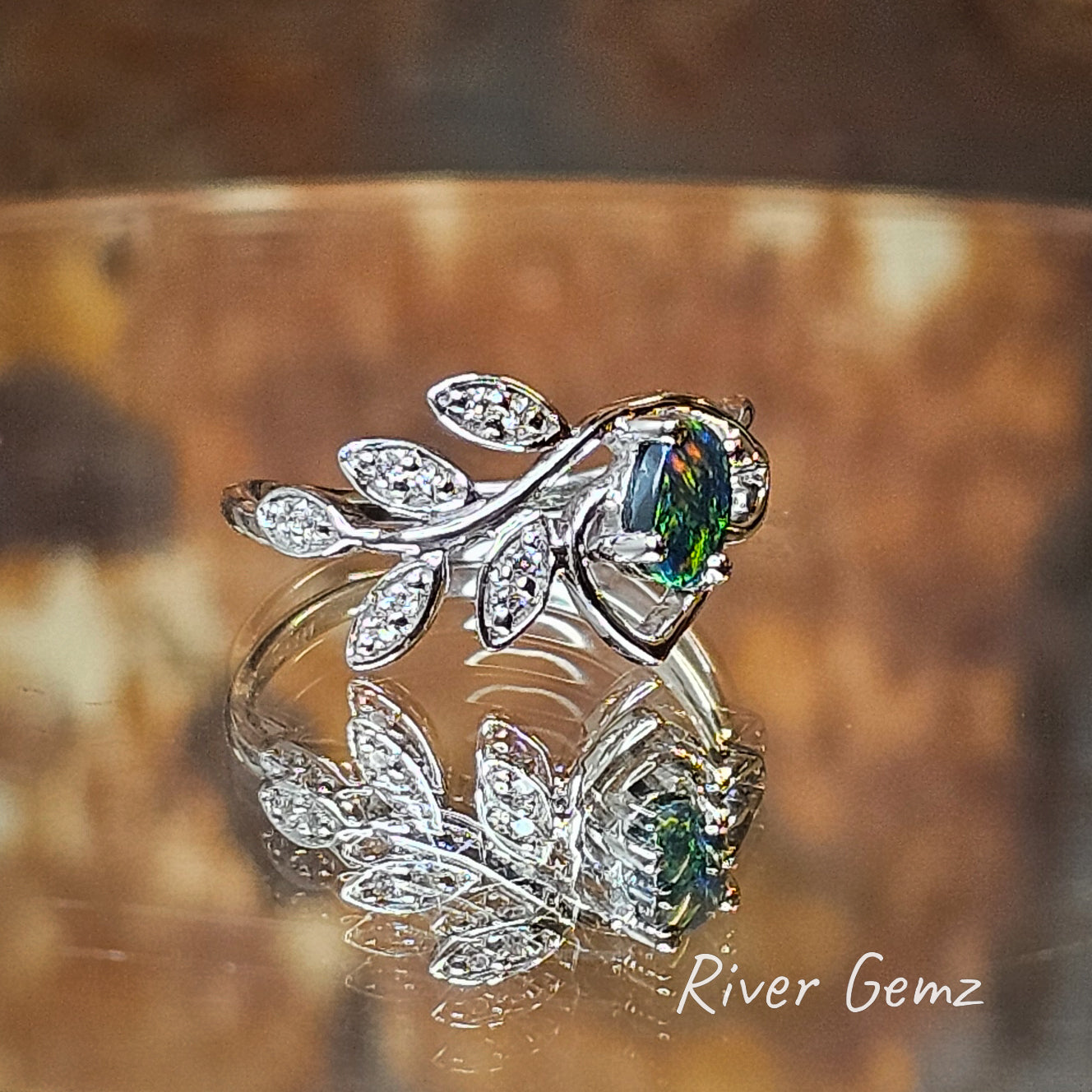 Black opal mainly green but with some orange flecks set in silver ring with 5 leaves adorned with white topaz.