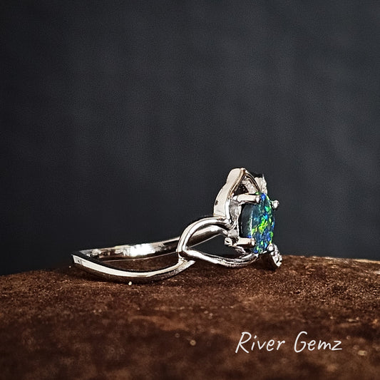 Silver ring with a blue & green black opal on a dark background, branded 'River Gemz'.